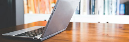 Open laptop on a table in front of a bookcase.