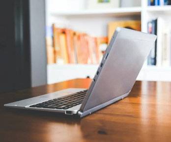 Open laptop on a table in front of a bookcase.