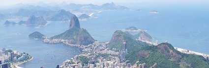 A view over Rio de Janeiro showing a sprawling city located in the valley between green wooded hills, finishing at the ocean