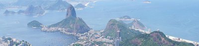 A view over Rio de Janeiro showing a sprawling city located in the valley between green wooded hills, finishing at the ocean