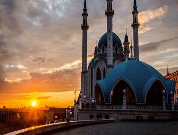 The sun is setting over ornate Russian buildings, which have arched windows, thin towers and turrets