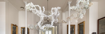 Art sculpture made of braided shredded paper, hanging in an ornate room with wooden floors and oil painting portraits