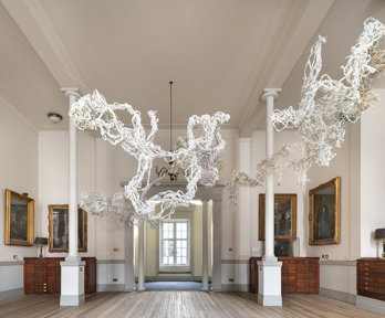 Art sculpture made of braided shredded paper, hanging in an ornate room with wooden floors and oil painting portraits
