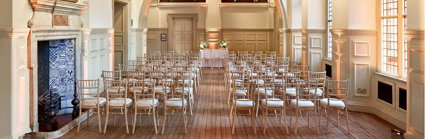 Wooden chairs setup for a wedding ceremony underneath the arch in the Main Hall.