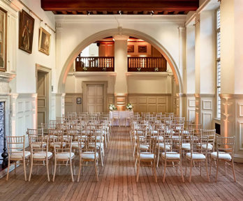 Wooden chairs setup for a wedding ceremony underneath the arch in the Main Hall.