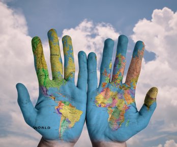 Hands that have a world map projected on to them, showing palm side round. The background is a cloudy blue sky