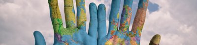 Hands that have a world map projected on to them, showing palm side round. The background is a cloudy blue sky