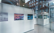 View through a glass window of a photographic exhibition displayed on white panels.