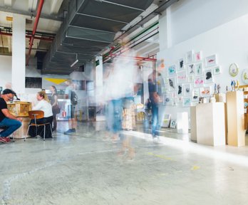 People moving around an exhibition with artwork hung on the walls and sculptures on stands.