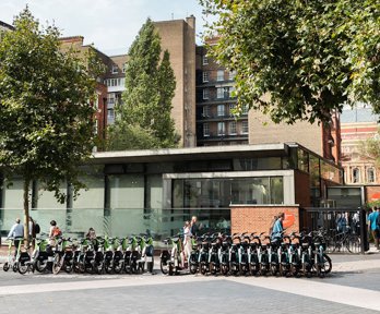 The Society's pavilion as people enter through the gate to the main entrance. In front of the entrance is a row of rentable e-bikes.