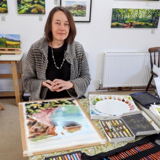 Anna Brewster in her studio sitting in front of one of her artworks depicting a landscape.