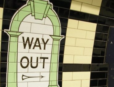 Tiled 'way out' sign pointing towards the exit on a train station platform.