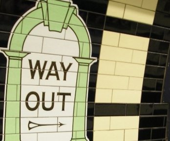 Tiled 'way out' sign pointing towards the exit on a train station platform.