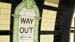 Tiled 'way out' sign pointing towards the exit on a train station platform.