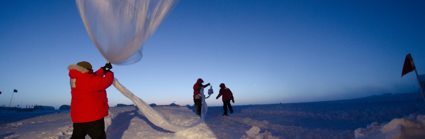 Three people undertake nondescript research in a seemingly artic environment. The snowy landscape stretches as far as the eyes can see