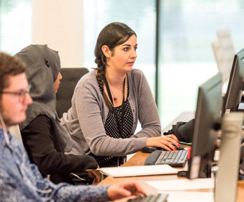 Three people working at a desk and looking at computer screens.