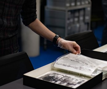 A researcher wearing archival gloves viewing historic photographs in a folder