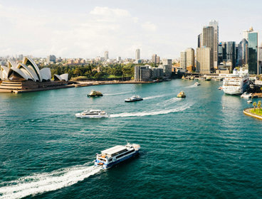 A skyline view of Sydney, Australia, as seen from the sea, showing boats and the Sydney Opera House.