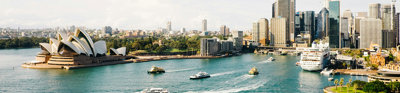 A skyline view of Sydney, Australia, as seen from the sea, showing boats and the Sydney Opera House.