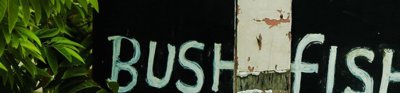 A large black sign with white painted words, spelling out 'wild meat' and 'bush Fish for sale'.