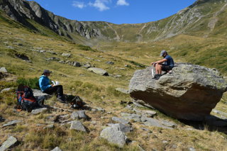 Two researchers sat in a valley, one on the ground and the other on a boulder, writing notes.