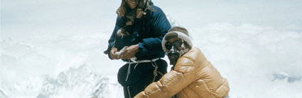 Two expeditioners in winter gear in a snowstorm on top of a snowy mountain.