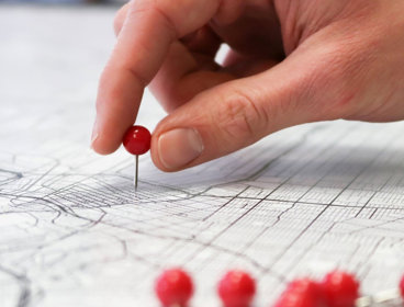 Close-up of a person's hand pushing a push pin into a map of a city.