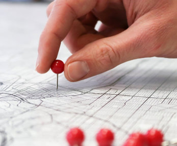 Close-up of a person's hand pushing a push pin into a map of a city.