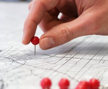 Person pushing a push pin into a map of a city.