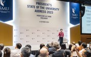 A woman on a stage below a sign that says President's State of the University Address 2023, giving an address to an audience.