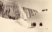Black and white photograph of Niagara Falls with people standing in snow and viewing the waterfall from below.