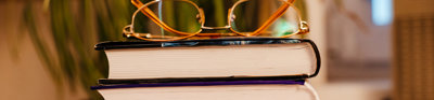 A pair of glasses rest on a stack of five books are stacked on top of each other.