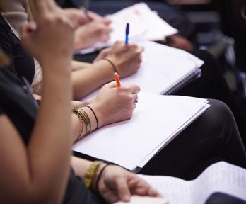 Seated people taking notes using notebooks