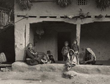 Black and white image of adults and children sat outside a typical Limbu house in Eastern Nepal. Photographer: C.J.Morris, 1926
