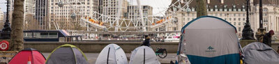 A row of tents pitched on the road, with the London Eye in the background.