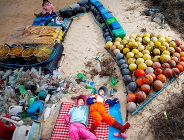 Earth Photo 2023 entry combing the sea, combing peace. Two young people lie amongst sand and plastic from the ocean.