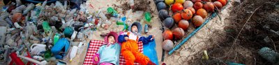 Earth Photo 2023 entry combing the sea, combing peace. Two young people lie amongst sand and plastic from the ocean.