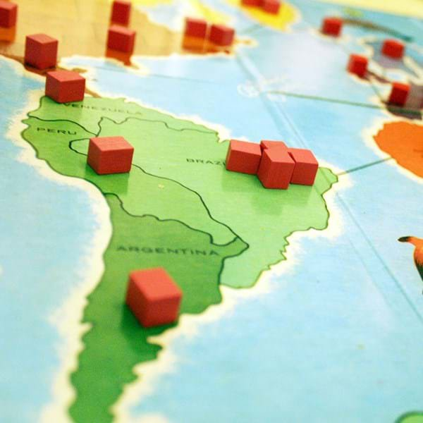 A close up of a board game on a table, depicting small red cubes on a map of South America