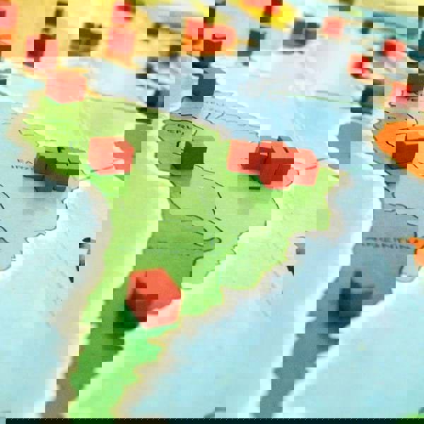 A close up of a board game on a table, depicting small red cubes on a map of South America