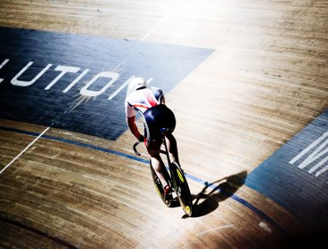 A cyclist in a union jack tunic riding a bicycle around a velodrome track