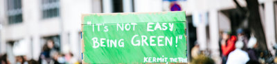 A person holding a sign saying 'Its Not Easy Being Green!' at a protest.