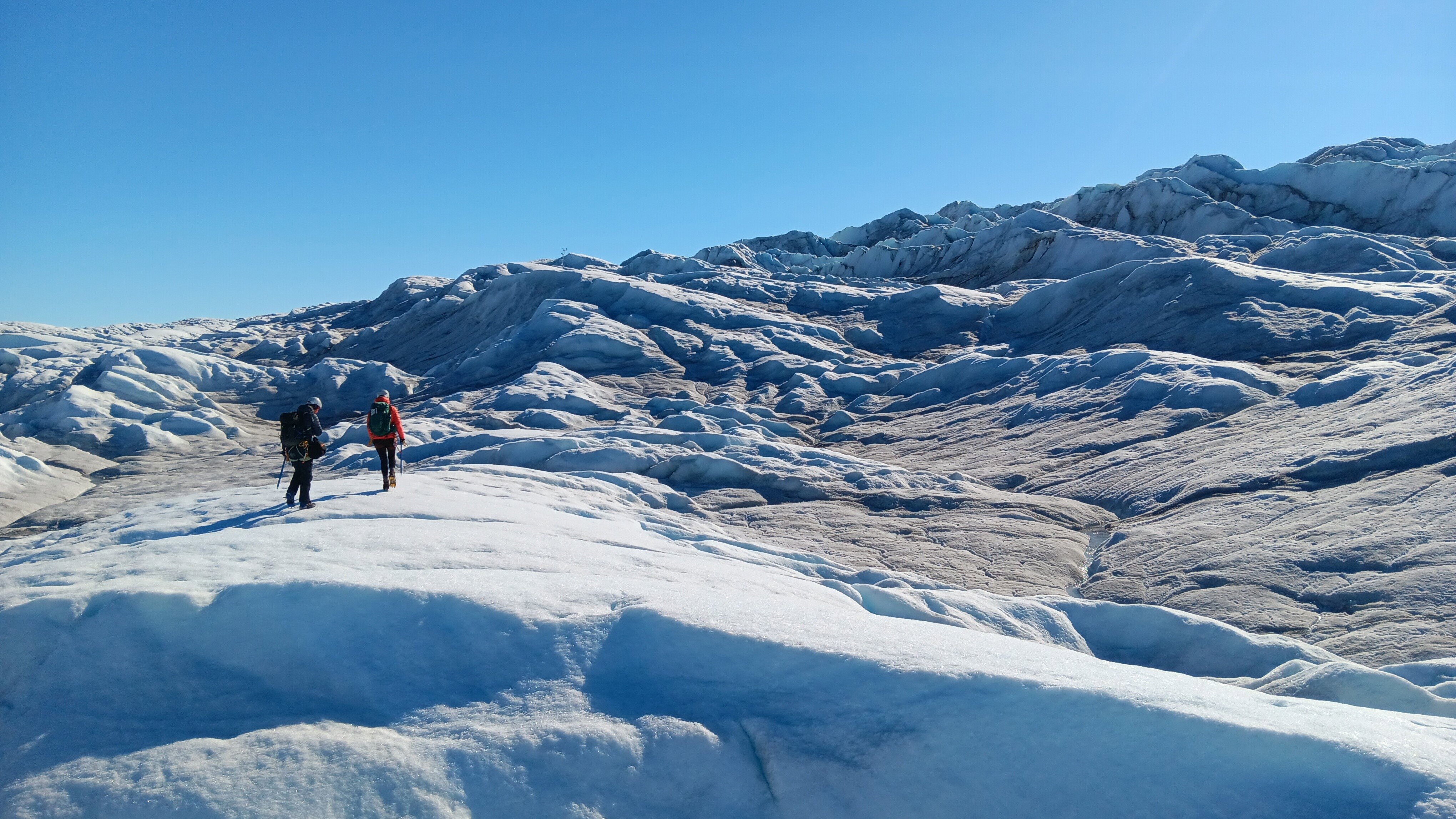 Photo from the Melting Ice And Changing Winds expedition of two trekkers crossing a rugged ice sheet in Greenland.