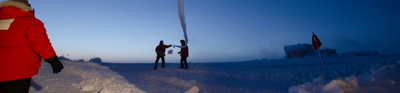 Two researchers stand in the distance holding research equipment. the are standing in a snowy artic landscape