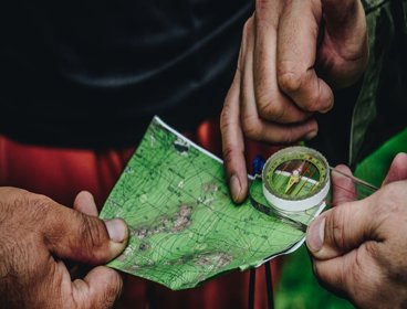 Hands holding a small map and compass. The map is mainly green and you can see contour lines on it