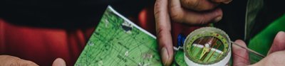 Hands holding a small map and compass. The map is mainly green and you can see contour lines on it