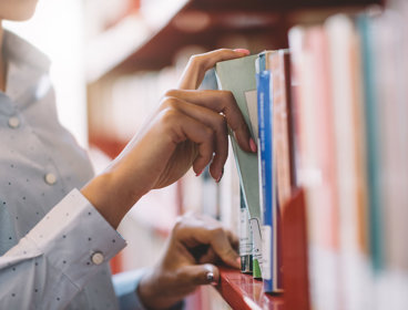 Close up of person taking a book from a shelf in a library.