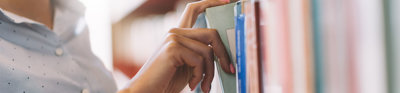 Close up of person taking a book from a shelf in a library.