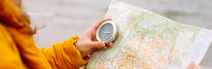 Close up of a person in a bright yellow coat holding a map and a compass.