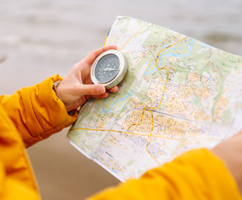 Close up of a person in a bright yellow coat holding a map and a compass.