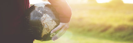 A person holding a small globe in their hand, down by their side. The sun is low in the sky and the light is bouncing off the top of the globe